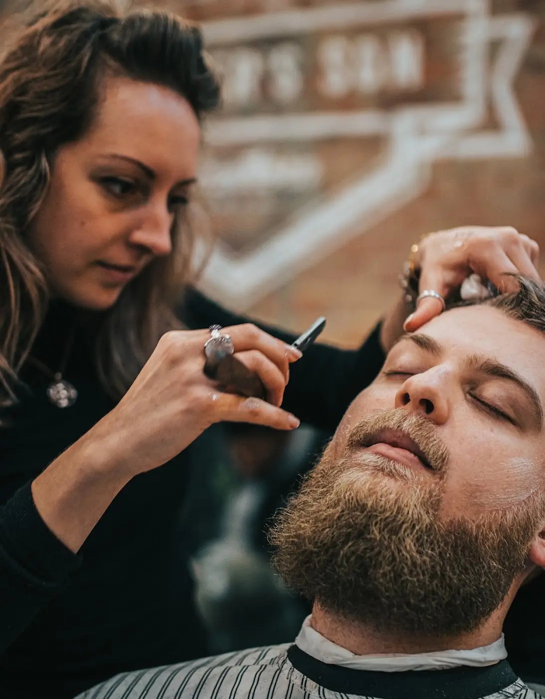 A barber shaping a client's beard with a straight razor